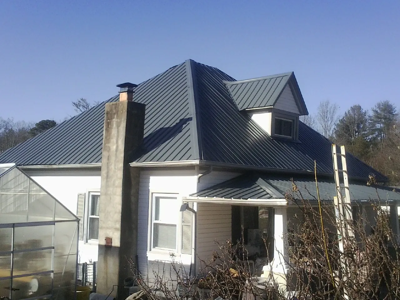 Dark blue standing seam metal roof on a white farmhouse with dormer — Slate & Tile Roof Repair by Roofing Brothers in Oakboro