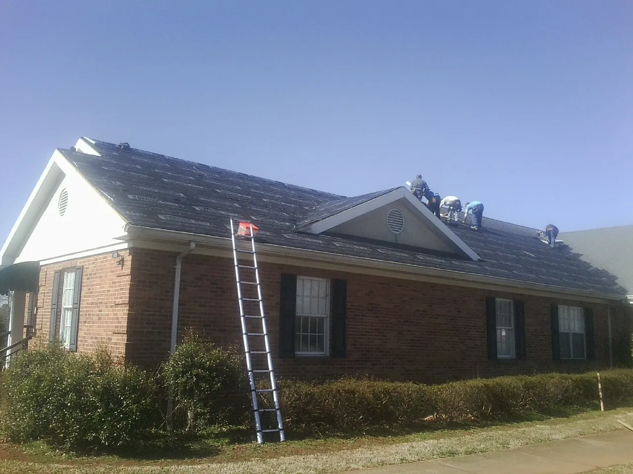 Crew tearing shingles off a brick ranch roof with a ladder set — Emergency Roof Repair work by our crew in Oakboro