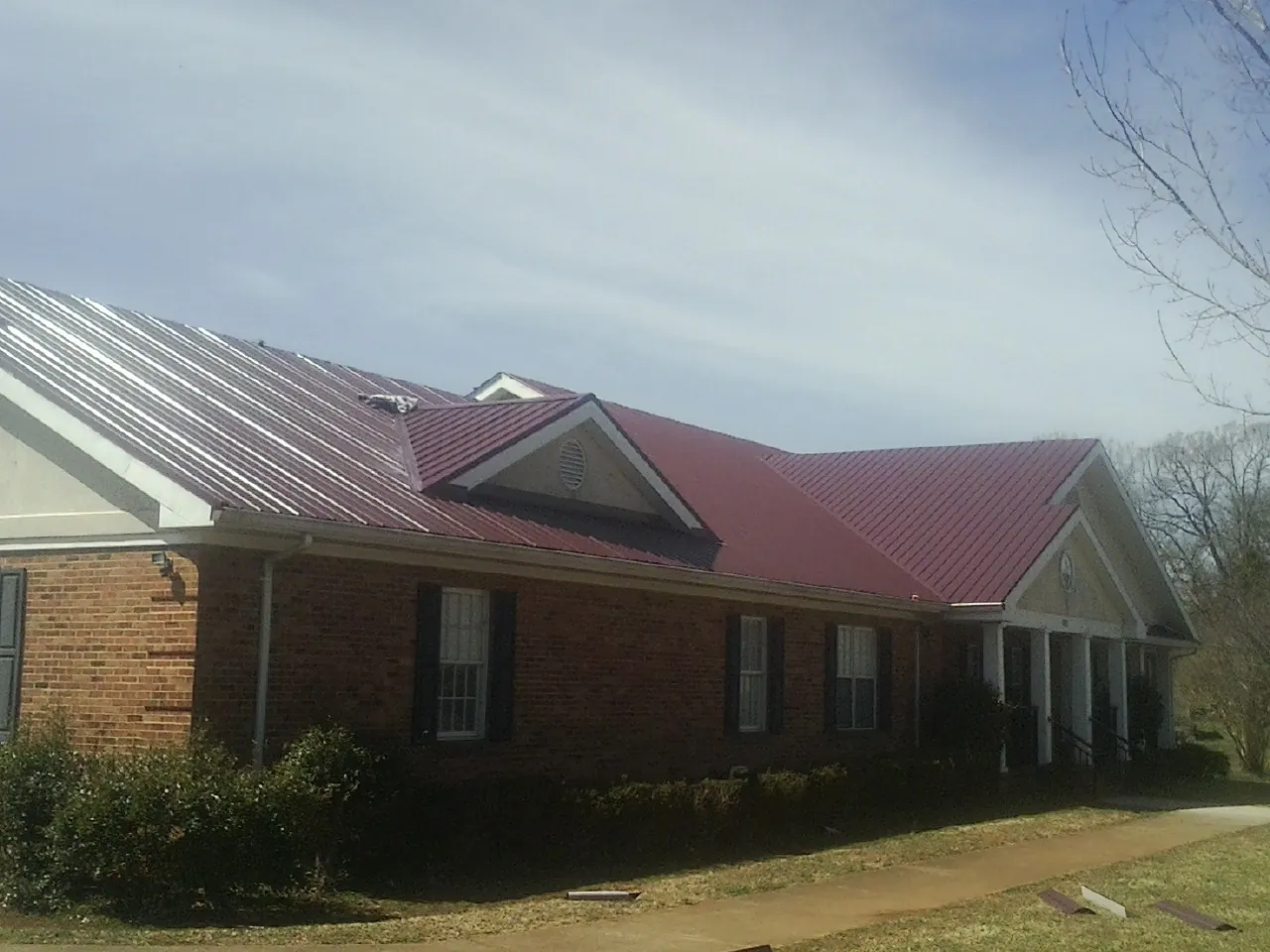 Red metal roof with gabled entries on a long brick building, from a Hail Damage Roof Repair job in Oakboro