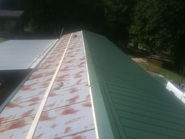Old rusted panels beside newly installed green metal roofing — Wind Damage Roof Repair by Roofing Brothers in Oakboro