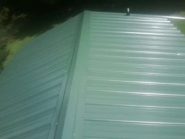New green metal panels meeting at the ridge of a roof — Flat Roof Repair work by our crew in Oakboro