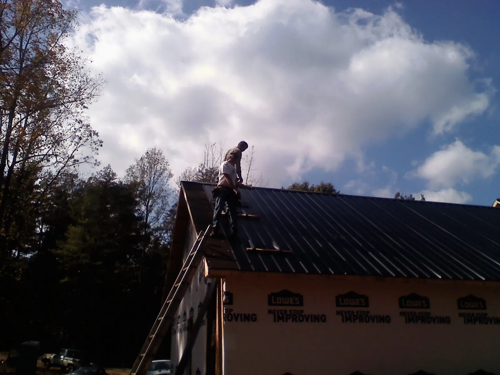 Roofer fastening dark metal panels high against a cloudy sky, from a Roof Inspection job in Oakboro
