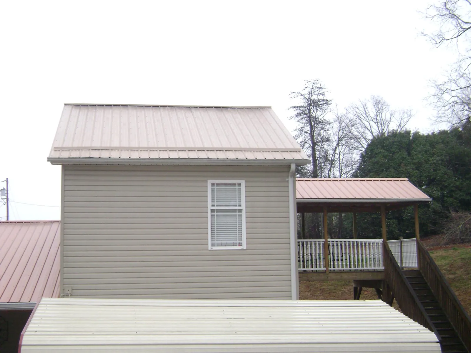 Tan metal roofs on a two story addition and attached porch, from a Roof Replacement job in Oakboro